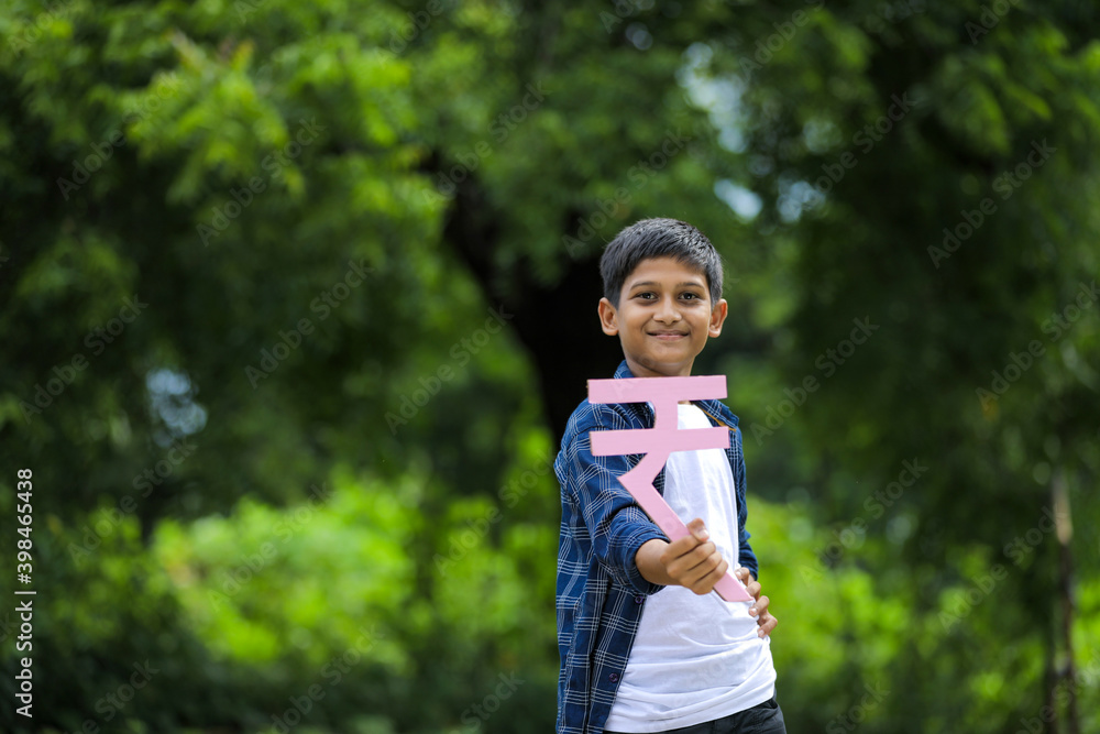 Cute indian little child holding indian rupees symbol in hand and showing expression Cute indian little child holding indian rupees symbol in hand and showing expression