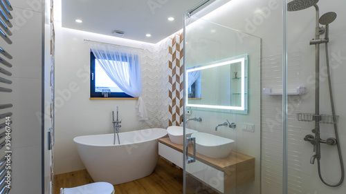 Contemporary interior of bathroom in luxary apartment. Double sink on countertop. White toilet and bathtub. Illuminated mirror. Shower.