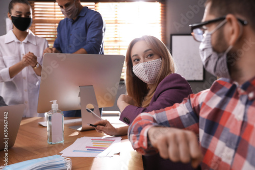 Coworkers with protective masks making elbow bump in office. Informal greeting during COVID-19 pandemic photo