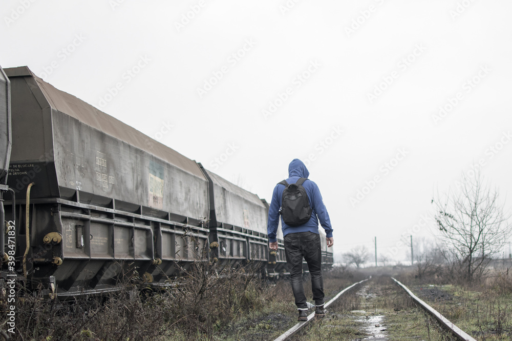 A man with a backpack walks on an industrial railway on a rainy day