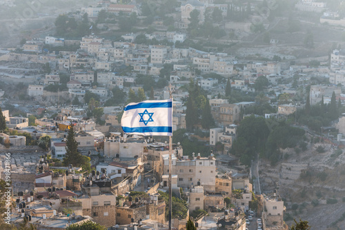 Israeli National flag waving on the top of Mount of Olive with background of residential houses in Jerusalem, Israel photo