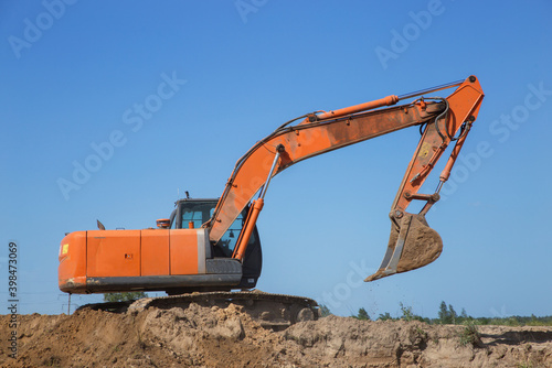 huge orange crawler excavator at work on earthen mountain in a sand quarry, on a sunny day against a blue sky. View from below