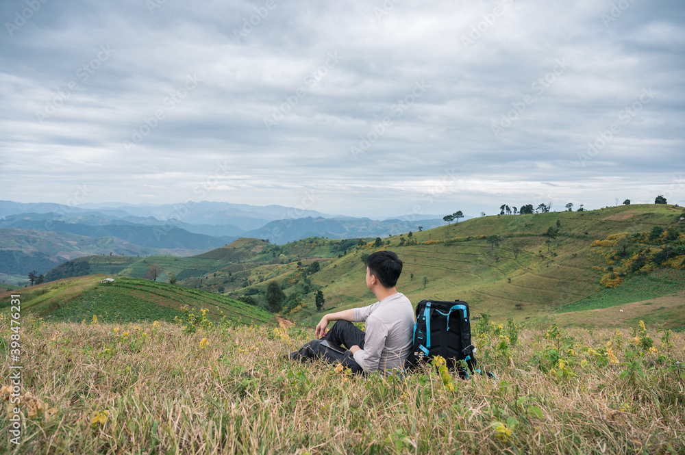 Asian man relaxing with camera bag on farmland hill in rural