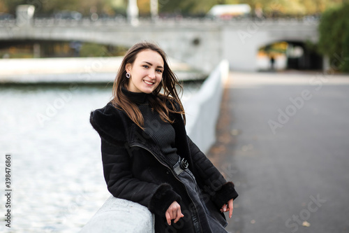 A girl stands on the embankment near the water, in warm clothes.