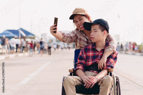Asian Disabled child on wheelchair and mother in the outdoors nature fun with selfie by smart phone,Life in the education age of special children,Happy disability kid travel in family holiday concept.