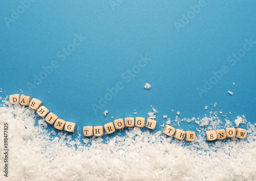 Small wooden block s with the inscription Dashing through the snow with snowflakes on a blue background