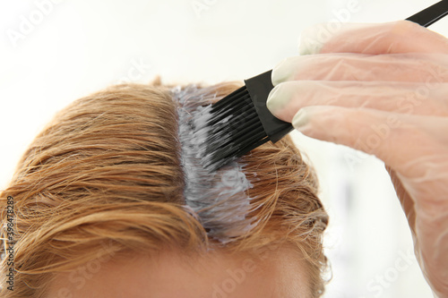 Young woman applying dye on hairs indoors, closeup