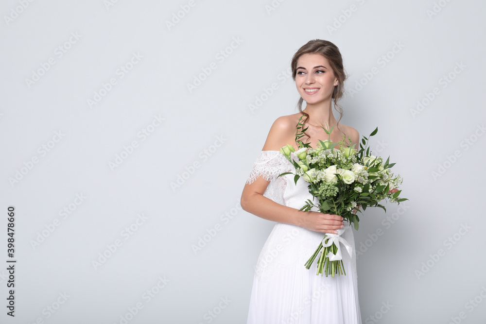 Young bride wearing wedding dress with beautiful bouquet on light grey background. Space for text Young bride wearing wedding dress with beautiful bouquet on light grey background. Space for text