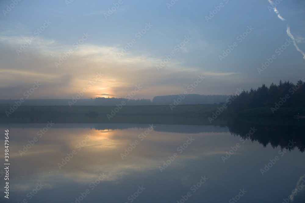 Contrails and conifer forest at the edge of a reservoir sunset image