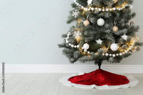 Decorated Christmas tree with red skirt indoors, space for text