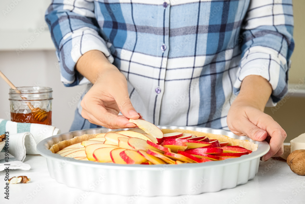 Woman putting apple slices into baking dish with dough to make traditional English pie at white table, closeup Woman putting apple slices into baking dish with dough to make traditional English pie at white table, closeup