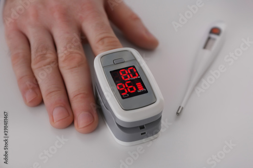 Man measuring oxygen level with modern fingertip pulse oximeter at white table, closeup