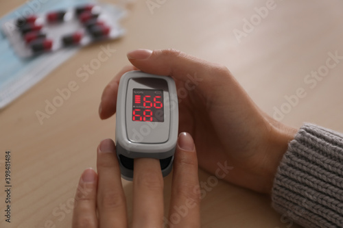Woman measuring oxygen level with modern fingertip pulse oximeter at wooden table, closeup