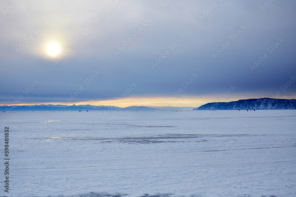 Beautiful sunset on the frozen lake Baikal. Listvyanka village in winter. Endless expanses of frozen lake covered with snow