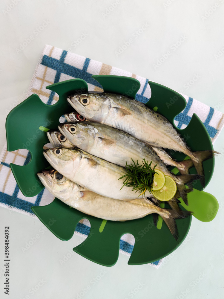 Fresh Indian Mackerel Fish Decorated with herbs on a green bowl,White Background.Selective focus. Fresh Indian Mackerel Fish Decorated with herbs on a green bowl,White Background.Selective focus.