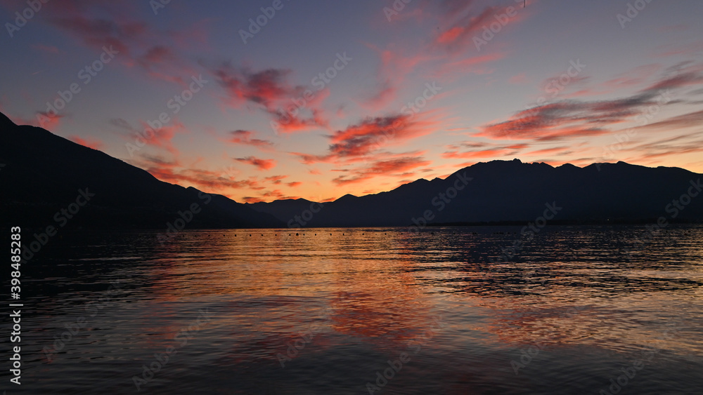 Suggestivo tramonto sul lago in autunno, con nuvole colorate di rosa, rosso e arancione. Immagine molto bella. 
