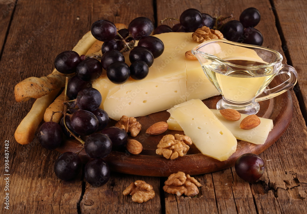 Gruyere cheese on a wooden table with grapes, nuts and olive oil Gruyere cheese on a wooden table with grapes, nuts and olive oil