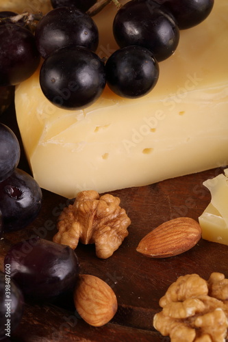 Gruyere cheese on a wooden table with grapes, nuts and olive oil