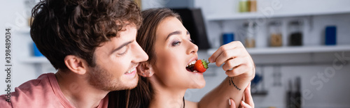 Smiling man feeding girlfriend with fresh strawberry, banner