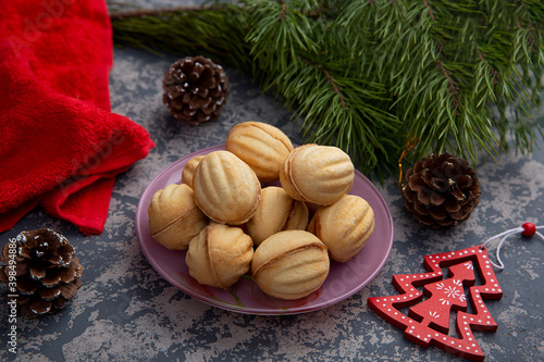 Delicious shortbread cookies in the shape of walnuts with a filling of sweet condensed milk and crushed nuts on the background of a Christmas tree and lights. Christmas treat. 