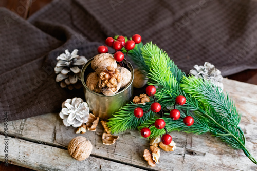 Walnuts in a tin, whole and split, next to the filling and shell. Presented in a New Year's composition with cones, red berries and a sprig of a Christmas tree. Home storage of winter preparations