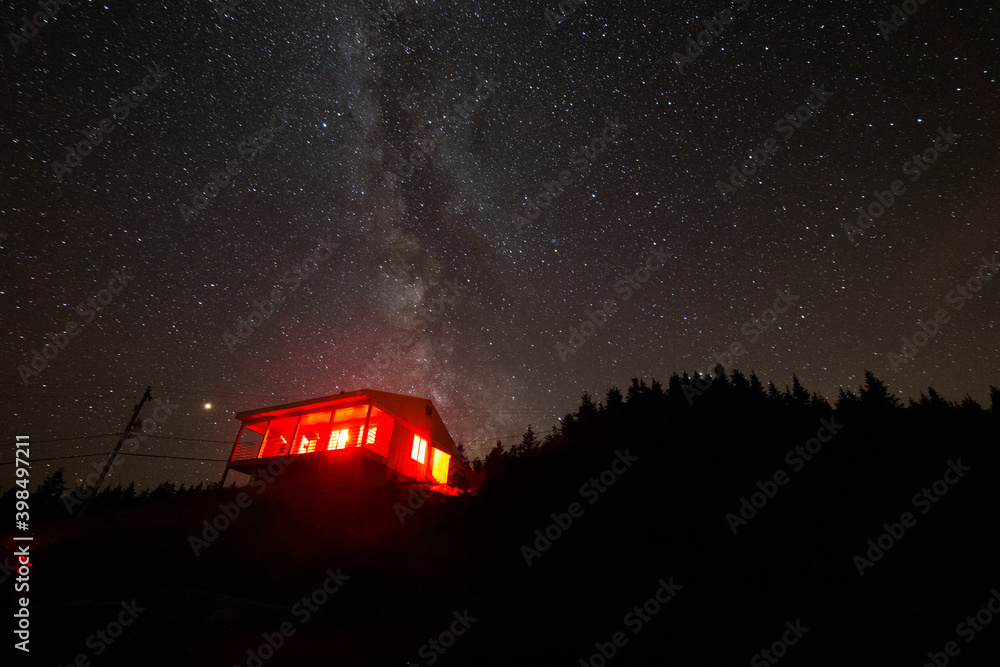 petite maison avec une lumière rouge au sommet d'une montagne avec la voie lactée en arrière plan
