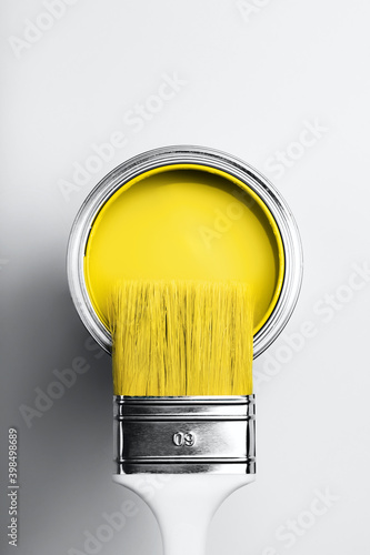 Demonstrating colors of year 2021 - Gray and Yellow. Brush with white handle on open can of yellow paint on monochrome background.