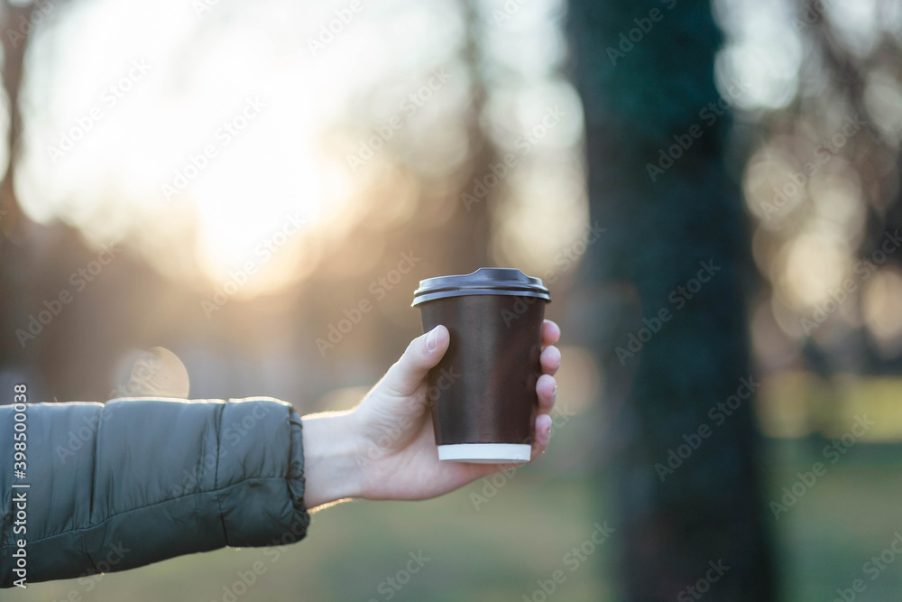 The guy holds a paper cup with coffee or tea. Have a cup of coffee. Disposable paper cup. Hot drink. Empty space. Man standing in the street holding a cup of coffee. Good morning. The guy holds a paper cup with coffee or tea. Have a cup of coffee. Disposable paper cup. Hot drink. Empty space. Man standing in the street holding a cup of coffee. Good morning.