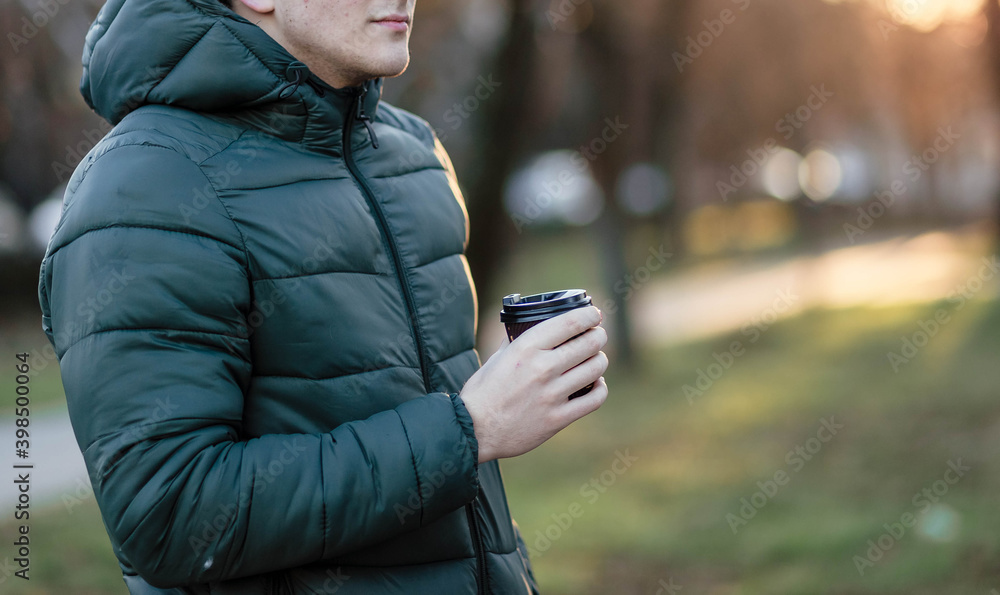 The guy holds a paper cup with coffee or tea. Have a cup of coffee. Disposable paper cup. Hot drink. Empty space. Man standing in the street holding a cup of coffee. Good morning. The guy holds a paper cup with coffee or tea. Have a cup of coffee. Disposable paper cup. Hot drink. Empty space. Man standing in the street holding a cup of coffee. Good morning.