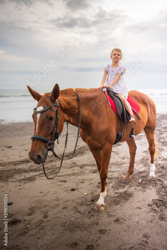 Pretty little girl riding horse on the beach. Happy childhood. Sunset time by the sea. Outdoor activities. Vacation concept. Bali, Indonesia
