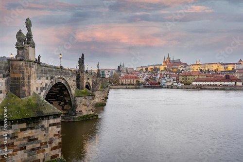 Prague Castle and St. Vitus Cathedral and the flowing Vltava River and statues and a street lamp on Charles Bridge in the center of Prague