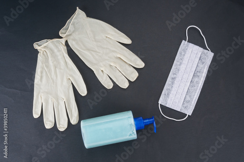 Medical mask, gloves and soap dispenser on black background