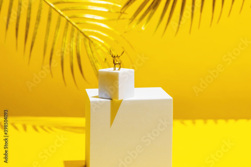 A small figure of a golden deer - a symbol of the new year on two white squares, in the style of monumentalism, on a yellow background, behind the leaves of a palm tree photo