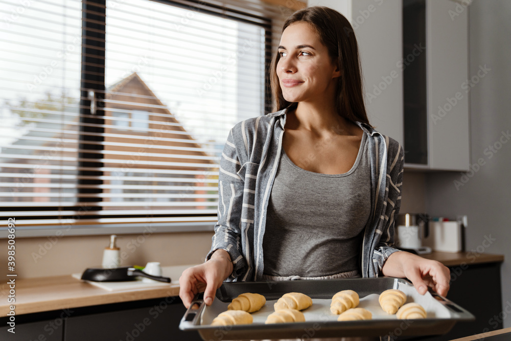 Charming happy woman smiling while cooking pastry in cozy kitchen