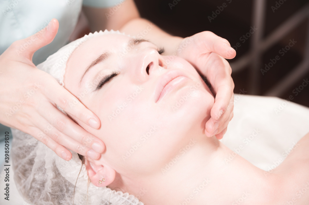 Professional masseur woman making facial massage in spa salon close-up.