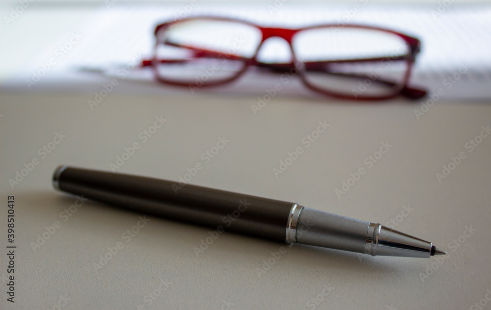 Work from home symbol. Metal pen and beautiful glasses on white document on a white table. Beautiful white background. Business and work from home concept. Work from home symbol. Metal pen and beautiful glasses on white document on a white table. Beautiful white background. Business and work from home concept.