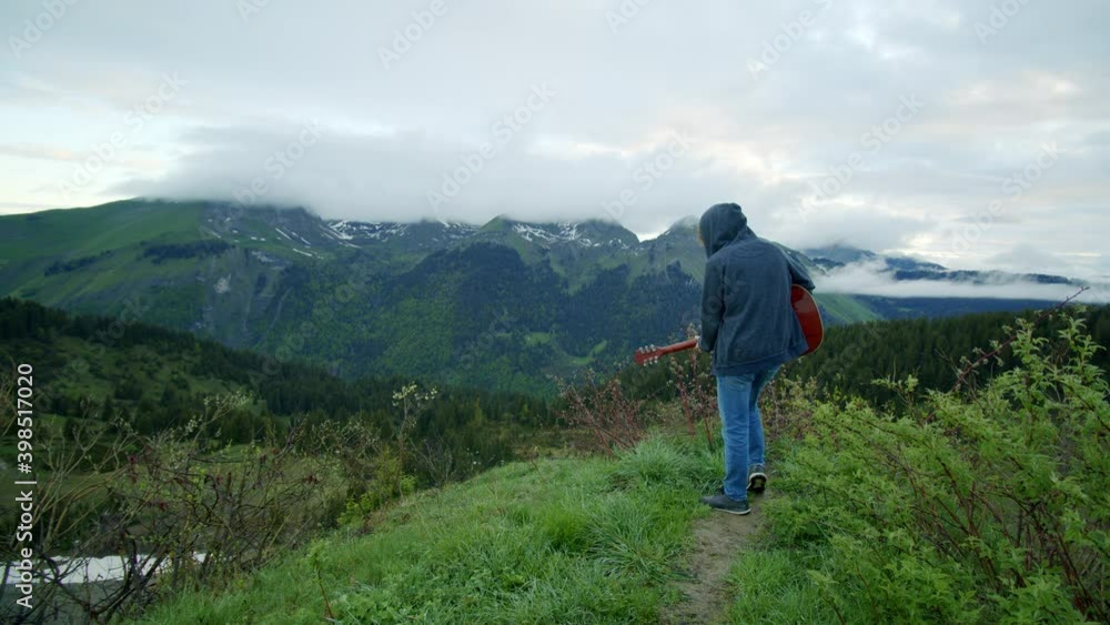 A man is playing the guitar at the top of a mountain under a moody sky A man is playing the guitar at the top of a mountain under a moody sky
