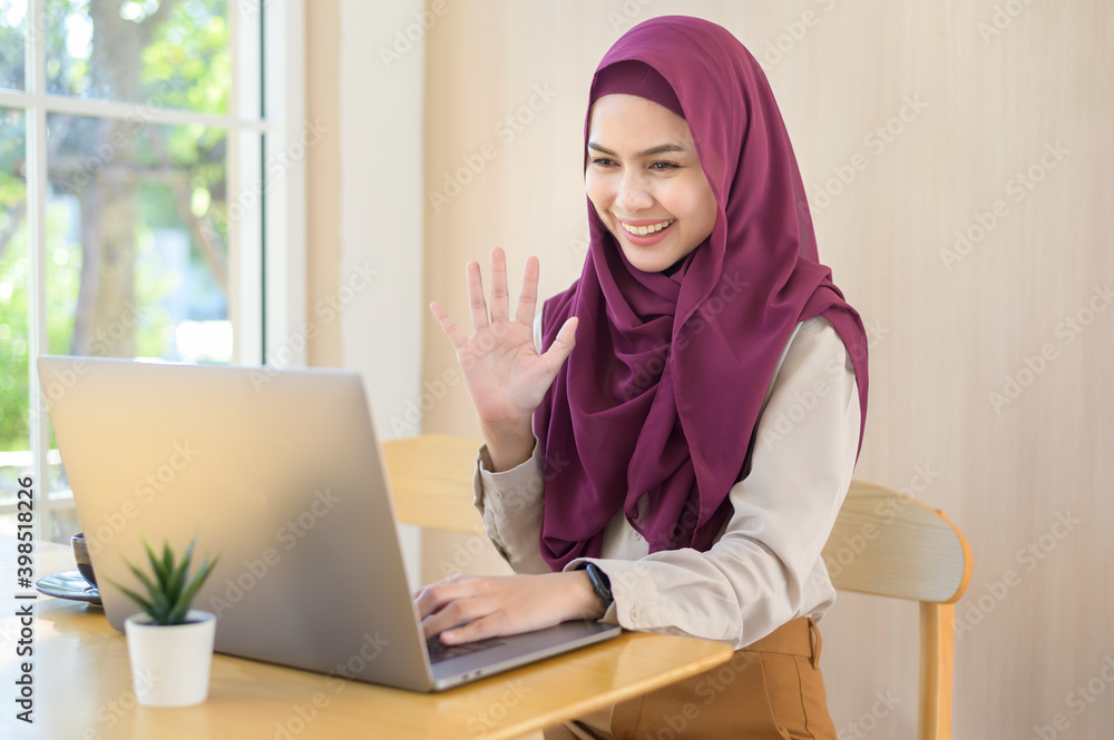 Muslim business woman in earphones watching webinar on laptop and making a video call at workplace Muslim business woman in earphones watching webinar on laptop and making a video call at workplace