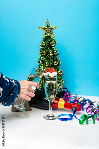 A hand holding champagne glass. Bottle of champagne and christmas tree with garlands on the background. Template for wallpaper  postcard  poster design  banner. Studio shot  high quality photo.