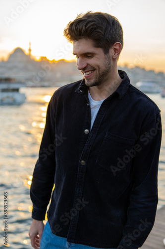 Young handsome man with a smile standing in Istanbul near Bosphorus on the sunset with a Mosque 