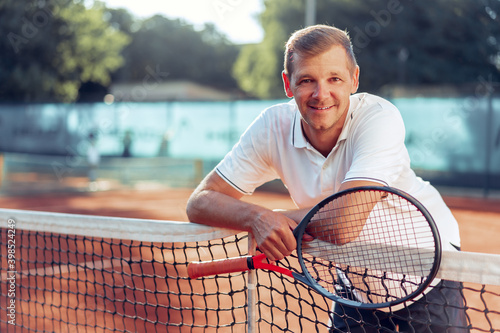 Portrait of positive male tennis player with racket standing at clay court © fotofabrika