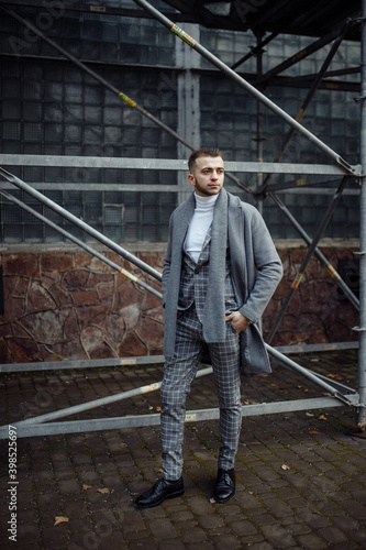 Full length body size photo ofcurious young man in stylish outfit wearing plaid suit grey coat scarf 