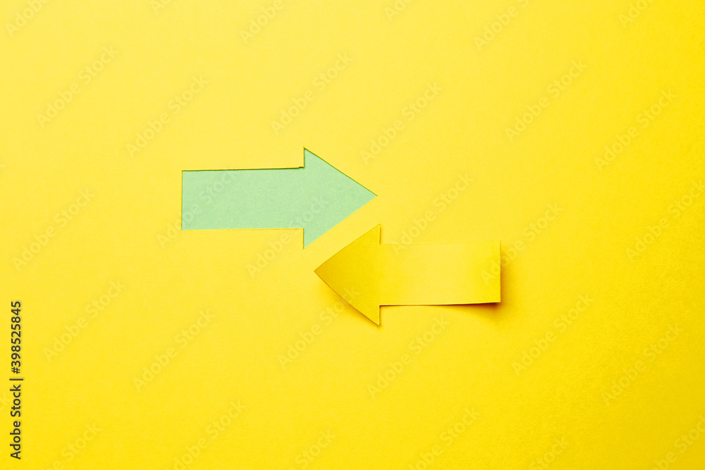 Two opposite left/right arrows, one cutted from the yellow paper curved up of two sides on the yellow paper background other made as an arrow shaped hole in the background with green paper underlay Two opposite left/right arrows, one cutted from the yellow paper curved up of two sides on the yellow paper background other made as an arrow shaped hole in the background with green paper underlay