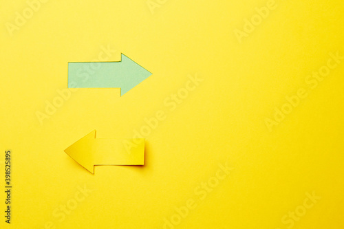 Two opposite left/right arrows, one cutted from the yellow paper curved up of two sides on the yellow paper background other made as an arrow shaped hole in the background with green paper underlay © Antonio