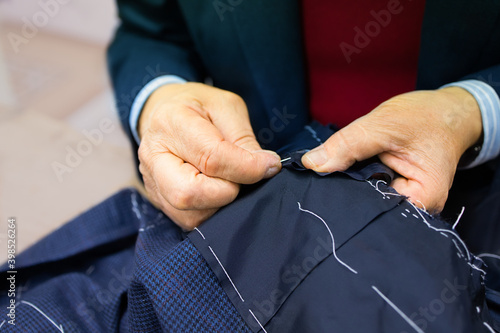 Bild auf Leinwand The hands of an elderly tailor basting and sewing the men's jacket