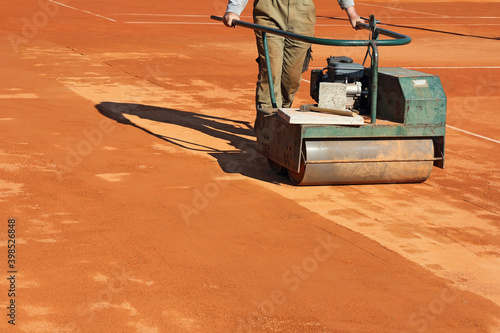 Worker with roller editing clay tennis court