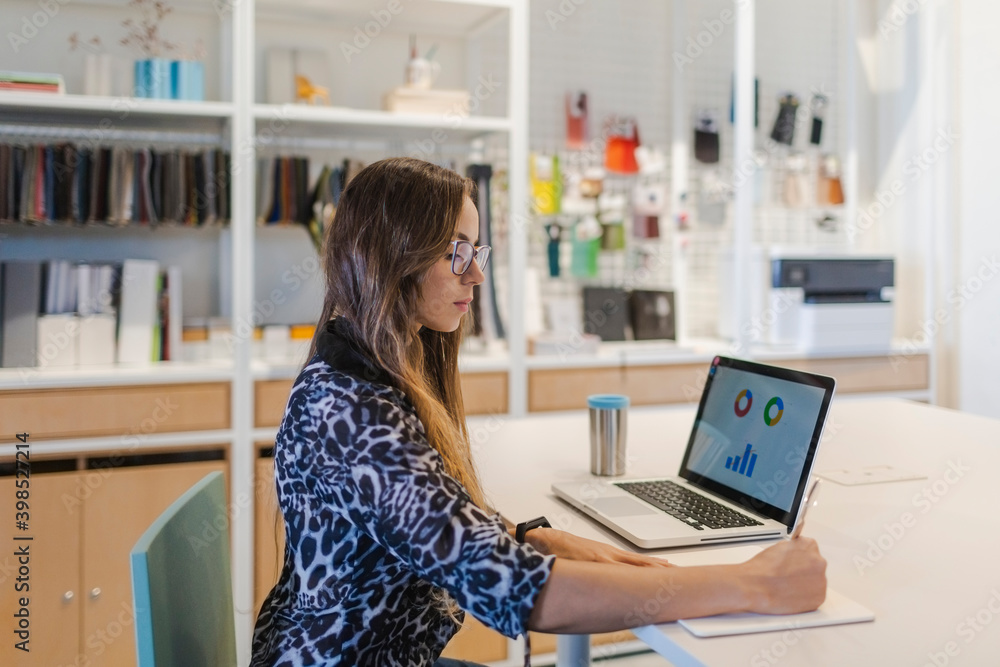Creative businesswoman writing in diary at desk in office Creative businesswoman writing in diary at desk in office