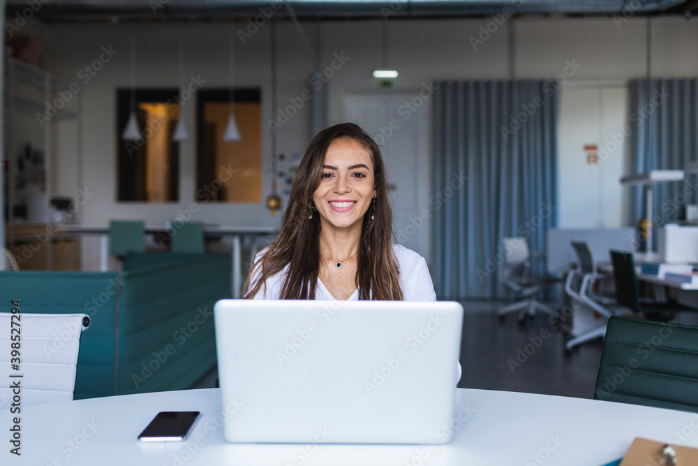 Smiling businesswoman with laptop at desk in office Smiling businesswoman with laptop at desk in office