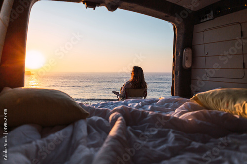 Woman admiring sunset view while while sitting on chair by camper van at beach