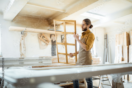 Handsome carpenter checking the quality of the window frame before the paint at the carpentry workshop